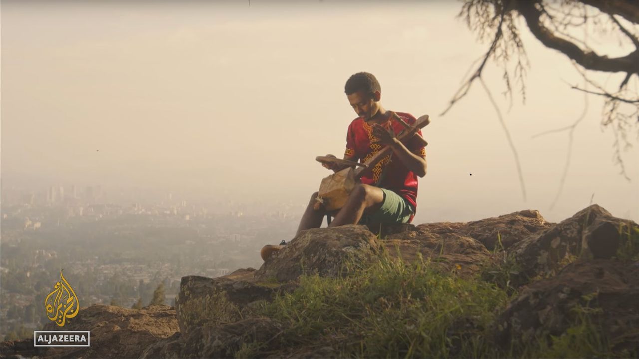 A young Ethiopian azmari musician plays the masenqo on a highland cliff edge above the Rift Valley at sunrise