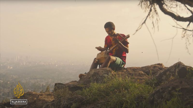 A young Ethiopian azmari musician plays the masenqo on a highland cliff edge above the Rift Valley at sunrise