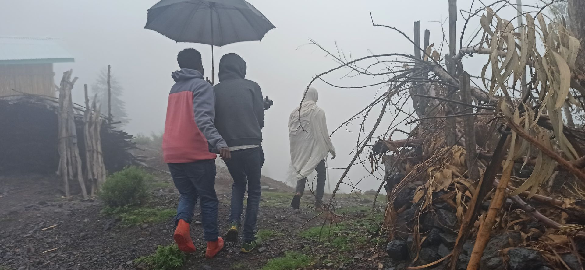 A documentary crew walks through thick highland fog under an umbrella while filming The Bookmaker in rural Ethiopia