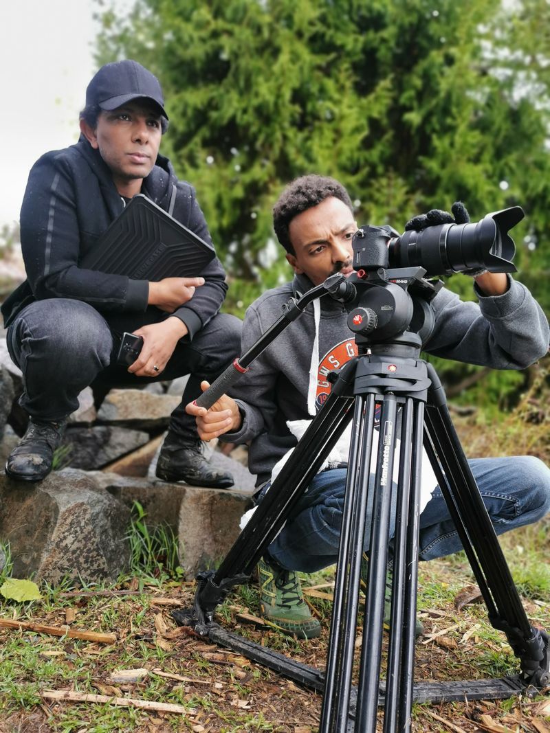 Two crew members set up a long lens on a tripod in Ethiopian forest during a documentary shoot