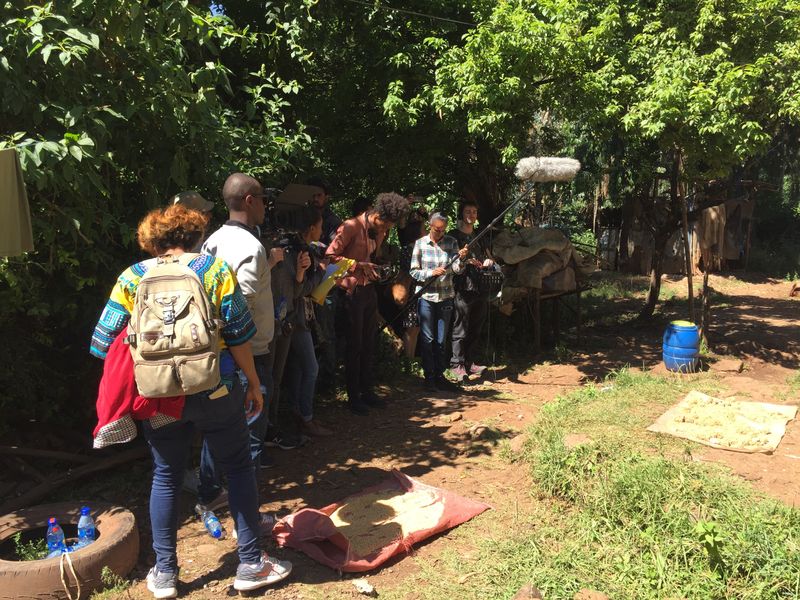 Crew and equipment staged under trees at a green outdoor filming location in Ethiopia