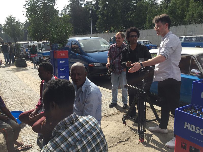 Production crew filming a street scene in Addis Ababa surrounded by onlookers and production vehicles