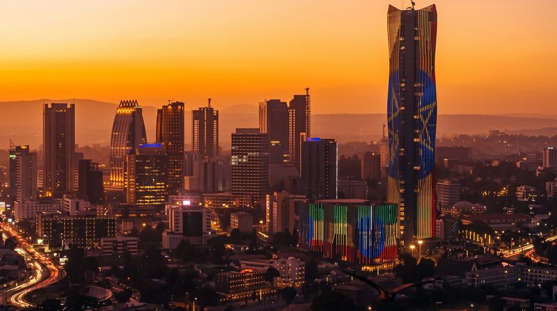 The Addis Ababa skyline at sunset, with the towers of the city's financial district lit against an orange sky